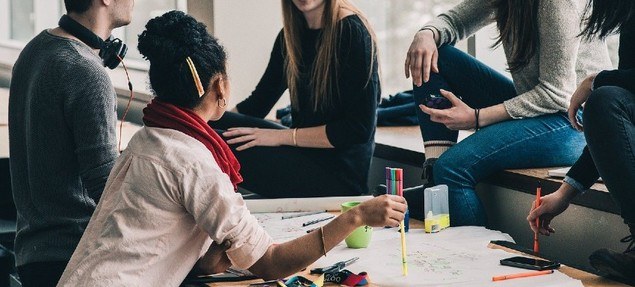 Young people gathered around a table talking | Old School Networking